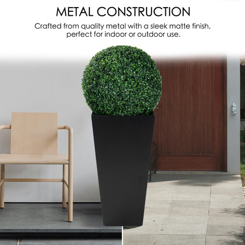 A tall, black metal taper planter with a sleek matte finish, holding a spherical green plant. Crafted from quality metal, it suits both indoor and outdoor settings, enhancing decor with a touch of greenery. Tall Taper Black Metal Planter - Quality Metal Construction. Tall taper planter, black metal, indoor - outdoor planters, metal construction.