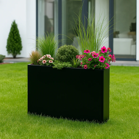 Decorative black outdoor planter box filled with colorful flowers, pink blooms, ornamental grasses, and greenery, displayed on a lush green lawn in a modern home garden.