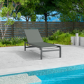 A gray outdoor lounge chair with a sleek black metal frame is positioned beside a swimming pool. The setting includes a wooden fence, green plants, and a concrete patio, creating a serene and relaxing outdoor environment. gray lounge chair, outdoor lounge chair, poolside furniture, black metal frame, relaxation.