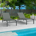 Two gray outdoor lounge chairs with dark frames are positioned beside a swimming pool. The background includes greenery and a wooden fence, creating a relaxing outdoor setting. gray outdoor lounge chairs, poolside furniture, outdoor relaxation, dark-framed lounge chairs.