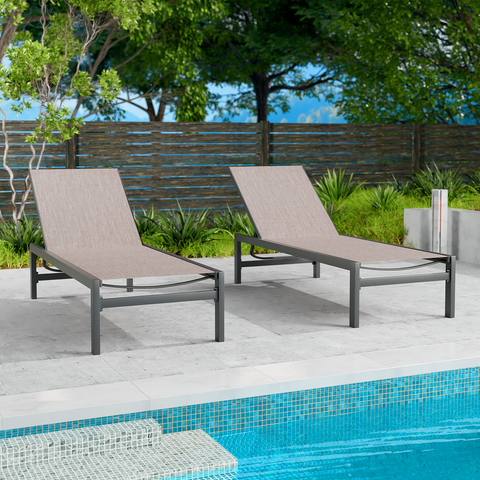 Two beige outdoor lounge chairs with dark frames are positioned beside a swimming pool. The background includes greenery and a wooden fence, creating a relaxing outdoor setting. Beige Outdoor Lounge Chairs: Relax by the Poolside.beige outdoor lounge chairs, poolside furniture, outdoor relaxation, dark - framed lounge chairs