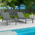 Two gray outdoor lounge chairs with dark frames are positioned beside a swimming pool. The background includes greenery and a wooden fence, creating a relaxing outdoor setting. gray outdoor lounge chairs, poolside furniture, outdoor relaxation, dark-framed lounge chairs.