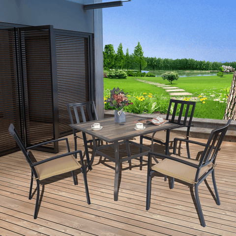 An outdoor dining setup featuring a square dining table with a brown - framed, rustic - looking tabletop. The table is surrounded by four chairs with beige cushions. Set on a wooden deck, the scene overlooks a picturesque landscape with greenery, a lake, and a clear blue sky. Outdoor Dining Table with Brown Frame: Enjoy Scenic Views. outdoor dining table, brown frame, wooden deck, beige - cushioned chairs, scenic landscape.