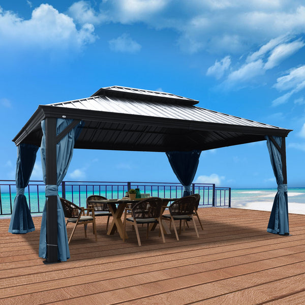 An outdoor hardtop gazebo with a sleek, metallic - looking roof is set on a wooden deck overlooking a beach scene with blue waters and a partly cloudy sky. The gazebo features elegant blue curtains that are tied back, and beneath it, there is a wooden table surrounded by wicker chairs, creating a cozy outdoor dining or lounging area.Beachside Outdoor Gazebo with Blue Curtains and Seating Area. outdoor gazebo, beach view, blue curtains, wooden deck, wicker chairs, hardtop gazebo.