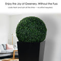 An artificial topiary ball in a black planter, placed indoors in a modern living room setting. The lush, green sphere offers the look of fresh greenery with no maintenance required, enhancing the decor effortlessly. Artificial Topiary Ball - Effortless Greenery Indoors. Artificial topiary ball, faux green plant sphere, low - maintenance greenery.