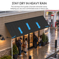 Kozyard 135 inch metal awning featuring an integrated front gutter system that channels rainwater toward the canopy edges during heavy rainfall. Installed above a commercial storefront entrance, this wall mounted outdoor rain canopy helps protect customers and entryways from direct rain exposure. Ideal for restaurant entrance awnings, commercial door canopies, exterior window covers, and residential rain shelters requiring extended overhead protection.