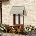 Kozyard 42-inch aluminum window awning and door canopy in beige metal panels with adjustable support arms, installed on a rustic stone wall over a double-hung window next to patio furniture and flowers. Perfect heavy-duty outdoor sun shade and rain protection for residential home improvement.
