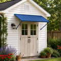 Kozyard 68-inch blue door awning installed on a white garden shed with double French doors, providing weather protection. The image captures the canopy over the wooden-style doors, surrounded by potted plants, lavender flowers, and a watering can, highlighting its aesthetic appeal and functionality in a residential garden setting.