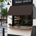 Kozyard brown metal awning installed over a coffee shop entrance, featuring a wide fixed canopy design for sun shade and rain protection. This wall mounted outdoor awning is ideal for storefronts, cafés, restaurants, windows, doors, patios and commercial entrances, combining durable powder-coated metal construction with a clean modern look for residential and commercial exterior use.