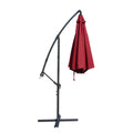 A side - view of a collapsed outdoor offset umbrella with a vibrant red canopy, mounted on a sturdy black stand with adjustable features. Folded Red Patio Umbrella: Compact and Sturdy Design. Collapsed Outdoor Umbrella: Red Canopy with Adjustable Stand. red patio umbrella, cantilever umbrella, folded umbrella, outdoor umbrella, adjustable stand, umbrella storage.