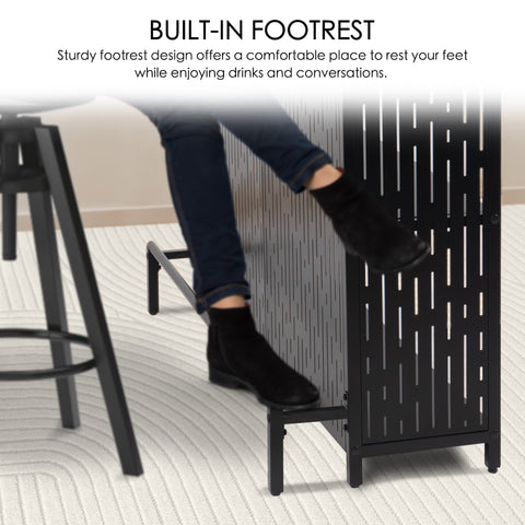 A black bar table with a built - in footrest. A person wearing jeans and black boots is shown resting their feet on the footrest, highlighting its sturdy design for comfort during drinks and conversations. Black Bar Table with Built - in Footrest. Bar table, built - in footrest, comfort.