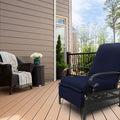 A navy blue-colored outdoor lounge chair with cushioned seating and armrests sits on a wooden deck. Adjacent to it is a wicker chair adorned with a striped throw blanket and a small wicker side table holding a vase of white flowers. The setting includes a house with siding, a railing, and a backdrop of trees.
Navy Blue Outdoor Lounge Chair for Relaxing on the Deck.
navy blue outdoor lounge chair, deck furniture, outdoor relaxation, cushioned seating