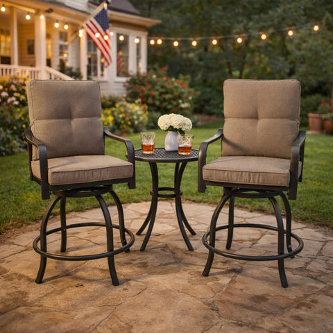 Kozyard swivel bar stools with cushions arranged around a matching small round bistro table with drinks on a paved stone patio backyard setup illuminated by warm outdoor string lights.