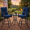 Kozyard swivel bar stools with cushions arranged around a matching small round bistro table with drinks on a paved stone patio backyard setup illuminated by warm outdoor string lights.