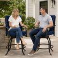 Kozyard modern outdoor swivel bar stools with armrests being enjoyed by a man and woman drinking wine and relaxing on a stylish apartment balcony overlooking urban residential buildings.