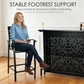 Indoor bar chair with stable footrest support, black wrought iron high bar stool providing comfortable seating beside a modern home bar unit, showing reinforced stability for kitchen or home bar furniture setups.