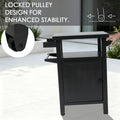 Kozyard movable outdoor prep table highlighting the locked pulley design for enhanced stability and safety. The diagram illustrates how the heavy-duty caster wheel locks securely to prevent the grilling cart from sliding during food preparation or BBQ cooking. A person's hand holds the side handle, demonstrating the smooth mobility and reliable stationary control of this gray metal patio utility cart.