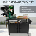 Kozyard ample storage capacity outdoor kitchen island highlighting versatile functionality. The open setup showcases stacked dinner plates, bowls, a beverage pitcher, glass cups, a wooden serving tray, and an apple basket on the tabletop and open middle shelf. A slide-out spice tray keeps utensils and refreshments organized, making this heavy-duty rolling bar cart perfect for hosting large garden parties.