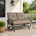 Kozyard outdoor patio glider bench featuring premium thick cushioned seating and a heavy-duty steel frame positioned on a cozy residential porch setting. This elegant two-seater loveseat rocker showcases a sophisticated design that seamlessly integrates into modern backyard patios, open decks, and lush garden landscapes. Designed for ultimate outdoor relaxation, the product highlights plush back support, deep seat comfort, and smooth gliding motion for contemporary home exteriors.