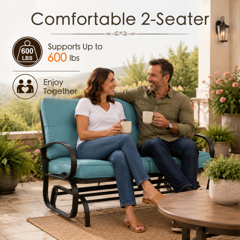 Lifestyle imagery showcasing a happy adult couple enjoying quality time together on a comfortable Kozyard two-seater porch glider bench. Sitting on an open-air residential veranda with a scenic valley view, they are holding mugs and smiling. The scene highlights the impressive six hundred pounds weight capacity and practical double seating layout of this premium glider rocker, illustrating an ideal relaxing afternoon experience for family members enjoying calm, gentle, rocking motion.