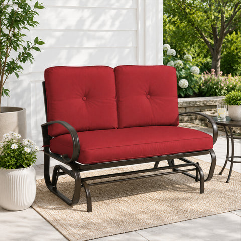 Kozyard outdoor patio glider bench featuring premium thick cushioned seating and a heavy-duty steel frame positioned on a cozy residential porch setting. This elegant two-seater loveseat rocker showcases a sophisticated design that seamlessly integrates into modern backyard patios, open decks, and lush garden landscapes. Designed for ultimate outdoor relaxation, the product highlights plush back support, deep seat comfort, and smooth gliding motion for contemporary home exteriors.