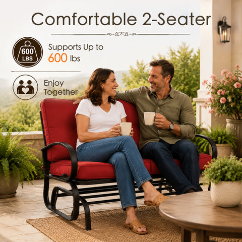 Lifestyle imagery showcasing a happy adult couple enjoying quality time together on a comfortable Kozyard two-seater porch glider bench. Sitting on an open-air residential veranda with a scenic valley view, they are holding mugs and smiling. The scene highlights the impressive six hundred pounds weight capacity and practical double seating layout of this premium glider rocker, illustrating an ideal relaxing afternoon experience for family members enjoying calm, gentle, rocking motion.