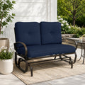 Kozyard outdoor patio glider bench featuring premium thick cushioned seating and a heavy-duty steel frame positioned on a cozy residential porch setting. This elegant two-seater loveseat rocker showcases a sophisticated design that seamlessly integrates into modern backyard patios, open decks, and lush garden landscapes. Designed for ultimate outdoor relaxation, the product highlights plush back support, deep seat comfort, and smooth gliding motion for contemporary home exteriors.