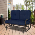 A glider chair with vibrant navy blue cushions is placed on a wooden deck, surrounded by a pleasant outdoor setting with greenery and a house facade in the background. The chair features a sturdy metal frame with curved armrests, providing a comfortable and stylish spot for relaxation.Navy Blue - Cushioned Glider Chair for Outdoor Relaxation.Navy blue - cushioned glider chair, outdoor furniture, metal frame, curved armrests, wooden deck
