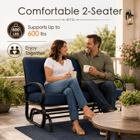 Lifestyle imagery showcasing a happy adult couple enjoying quality time together on a comfortable Kozyard two-seater porch glider bench. Sitting on an open-air residential veranda with a scenic valley view, they are holding mugs and smiling. The scene highlights the impressive six hundred pounds weight capacity and practical double seating layout of this premium glider rocker, illustrating an ideal relaxing afternoon experience for family members enjoying calm, gentle, rocking motion.