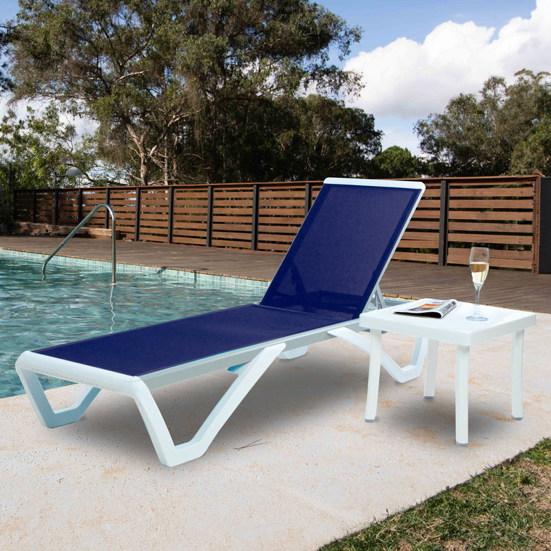 A serene outdoor scene features a stylish blue - cushioned lounge bed with a sleek white frame, placed beside a swimming pool. Next to the lounge bed is a matching white side table holding a glass of champagne and a magazine. The background includes a wooden fence and lush green trees under a partly cloudy sky.Relaxing Outdoor Lounge Set by the Pool. outdoor lounge bed, side table, swimming pool, blue cushion, white frame, relaxation.