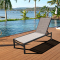 A beige - toned outdoor lounge chair with a black metal frame is positioned on a wooden deck by a pool, overlooking a scenic waterfront with palm trees, boats, and distant hills.Beige Outdoor Lounge Chair: Relax by the Pool with a View. beige outdoor lounge chair, poolside lounge chair, waterfront view, wooden deck furniture, black - framed lounge chair.