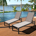 Two beige outdoor lounge chairs with black frames are set on a wooden deck by a swimming pool, with a picturesque view of a body of water, palm trees, and distant hills in the background.Beige Outdoor Lounge Chairs: Relax by the Pool with a Scenic View. beige outdoor lounge chairs, poolside loungers, scenic view, wooden deck furniture, black - framed lounge chairs. 