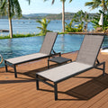 Two beige - toned outdoor lounge chairs with black frames are placed on a wooden deck beside a swimming pool, accompanied by a small black side table. The scenic background features palm trees, a body of water with boats, and distant hills. Beige Outdoor Lounge Chairs: Relax in Paradise by the Pool.beige outdoor lounge chairs, poolside loungers, wooden deck furniture, black - framed lounge chairs, outdoor relaxation.