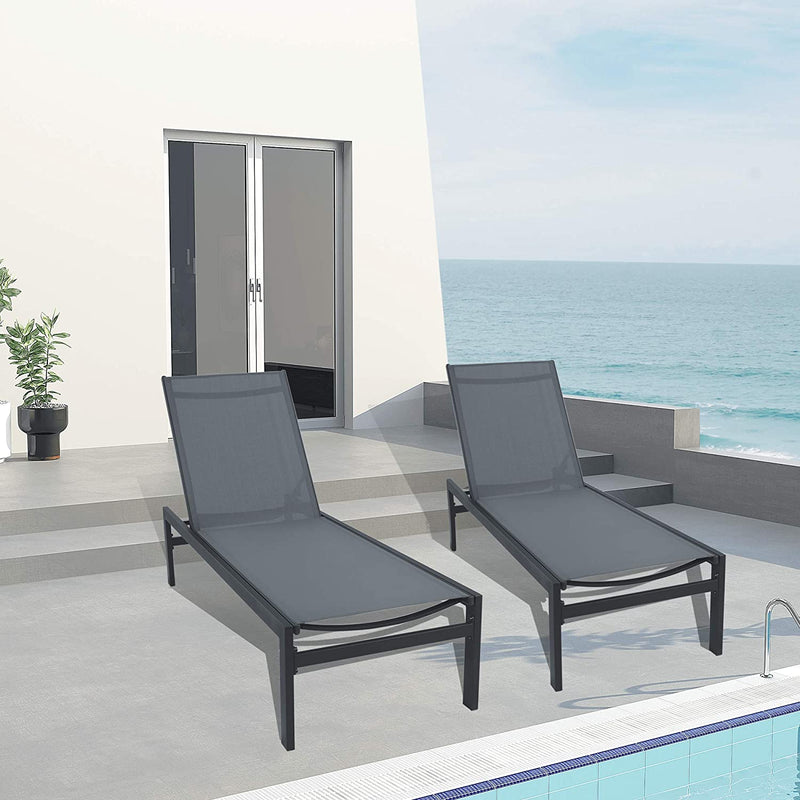 Two gray outdoor lounge chairs with black frames are placed on a concrete patio near a swimming pool, overlooking a serene sea view. The setting includes a modern white building with sliding glass doors and a potted plant, enhancing the relaxing atmosphere. Gray Outdoor Lounge Chairs: Relax by the Sea with Style. gray outdoor lounge chairs, black - framed lounge chairs, seaside relaxation, poolside furniture, modern patio chairs.