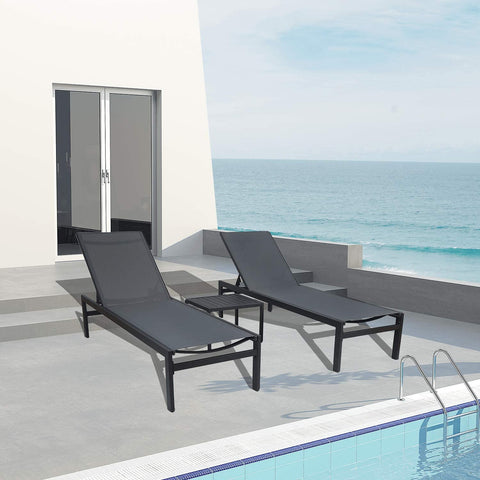 Two gray outdoor lounge chairs with black frames and a matching small side table are positioned on a concrete patio beside a swimming pool, with a stunning view of the sea in the background. The setting includes a modern white building with glass - paneled doors, enhancing the luxurious and relaxing atmosphere. Gray Outdoor Lounge Chairs: Relax by the Pool with a Sea View. gray outdoor lounge chairs, black - framed lounge chairs, poolside furniture, sea - view relaxation, outdoor side table.