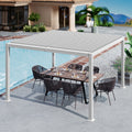 A modern white louvered pergola provides shade over an outdoor dining area beside a swimming pool. The setup includes a wooden dining table with wicker chairs, set against the backdrop of a luxurious house and lush greenery. White Louvered Pergola for Poolside Dining. louvered pergola, poolside, outdoor dining, white pergola, wicker chairs.