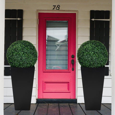 Two tall, black metal taper planters, each holding a lush spherical green plant, placed symmetrically on either side of a vibrant red front door numbered 78. Ideal for enhancing both indoor and outdoor aesthetics. Tall Taper Black Metal Planters for Front Door Decor. Tall taper planters, black metal, indoor - outdoor planters, front door decor. 