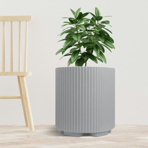 A sleek gray plastic planter pot with vertical ribbed texture holds a lush green plant. The planter is placed on a light - toned wooden floor next to a simple, light - colored wooden chair, set against a plain white background. The combination of the modern - looking pot and the natural greenery creates a stylish and minimalist indoor scene. Modern Gray Plastic Planter Pot: Stylish Indoor Greenery.gray plastic planter, ribbed planter pot, indoor plant pot, modern planter, minimalist planter.