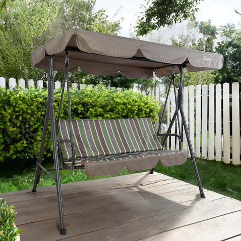 An outdoor swing chair set against a charming garden backdrop. The swing features a sturdy metal frame and a cushioned seat with green, brown, and white vertical stripes. Above, a beige canopy provides shade, branded with "Kozyard" on the corner. The swing is placed on a wooden deck, surrounded by lush greenery and a white picket fence, creating a serene and inviting atmosphere. Outdoor Swing Chair: Relax in Your Garden Oasis. outdoor swing chair, Kozyard swing, garden swing, swing with canopy, patio swing