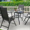 Outdoor Patio Dining Set
A square gray metal patio table with an umbrella hole, surrounded by four black folding chairs, set with a potted plant, teapot, cups, and a magazine, placed on a patio with greenery and a white picket fence in the background. Keywords: outdoor patio table, folding chairs, patio dining set