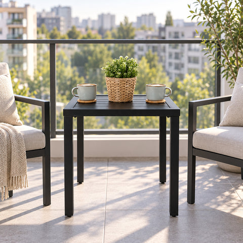 Kozyard black outdoor side table placed between patio chairs on a modern balcony, featuring a compact square slatted metal top and sturdy four-leg frame. This space-saving patio end table is ideal for coffee, drinks, plants and outdoor décor, making it a practical choice for apartments, balconies, decks, porches and small outdoor conversation areas.