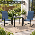 Kozyard compact black outdoor side table shown between two blue patio chairs on a covered porch, featuring a modern square slatted tabletop and sturdy metal legs. Perfect as a patio end table for drinks, plants and décor in gardens, decks, balconies and small outdoor spaces. Chairs are not included; image demonstrates table scale and versatile placement.