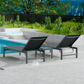 Two gray outdoor lounge chairs with dark metal frames are placed beside a swimming pool. The surrounding area features lush greenery and a wooden fence, creating a serene and inviting outdoor relaxation space. gray outdoor lounge chairs, poolside loungers, outdoor relaxation furniture, dark-framed lounge chairs.
