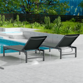 Two gray outdoor lounge chairs with dark metal frames are placed beside a swimming pool. The surrounding area features lush greenery and a wooden fence, creating a serene and inviting outdoor relaxation space. gray outdoor lounge chairs, poolside loungers, outdoor relaxation furniture, dark-framed lounge chairs.