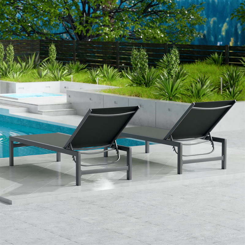 Two gray outdoor lounge chairs with dark metal frames are placed beside a swimming pool. The surrounding area features lush greenery and a wooden fence, creating a serene and inviting outdoor relaxation space. gray outdoor lounge chairs, poolside loungers, outdoor relaxation furniture, dark-framed lounge chairs.