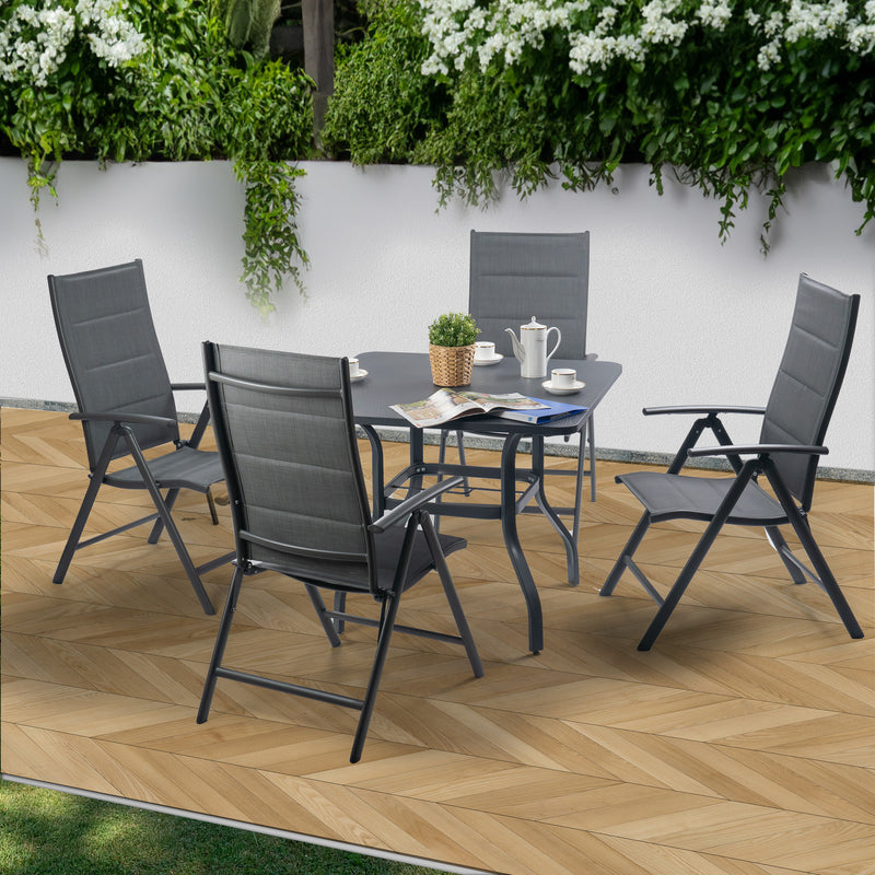 An outdoor patio furniture set featuring a square table and four folding chairs. The table is adorned with a coffee set, a small potted plant, and an open magazine. The chairs have a sleek design with dark gray fabric and black metal frames. Set against a backdrop of greenery and a white wall on a wooden - patterned floor, it creates a cozy outdoor relaxation spot. Cozy Outdoor Patio Table and Chair Set for Relaxation. outdoor patio furniture set, folding chairs, square patio table, dark gray fabric chairs.