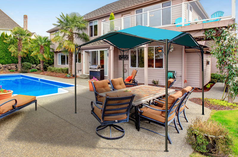 A KOZYARD Sun Shade Gazebo with a blue canopy is set up beside a backyard swimming pool, providing shade over an outdoor dining area with cushioned chairs and a table. The scene includes a two-story house in the background, enhancing the inviting outdoor living space. KOZYARD sun shade gazebo, blue canopy, backyard, swimming pool, outdoor dining, shade structure.