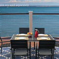 An outdoor dining scene featuring a rectangular composite wood dining table with a white frame, set against a stunning ocean view. The table is accompanied by black chairs with beige cushions, and there are place settings, a bowl of fruit, and a red pitcher on the table. Note: Chairs are sold separately. Rectangular Outdoor Dining Table with Ocean View (Chairs Sold Separately). rectangular outdoor dining table, composite wood table, white - framed table, outdoor chairs, ocean view dining