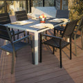 An outdoor dining setup featuring a rectangular composite wood dining table with a white frame, surrounded by six black outdoor chairs. The table is set with plates, napkins, and a bowl of fruit, placed on a wooden - deck patio with a scenic background. Rectangular Outdoor Dining Table with Chairs on Wooden Deck. rectangular dining table, composite wood table, outdoor dining set, white - framed table, wooden deck.