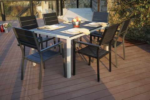 An outdoor dining setup featuring a rectangular composite wood dining table with a white frame, surrounded by six black outdoor chairs. The table is set with plates, napkins, and a bowl of fruit, placed on a wooden - deck patio with a scenic background. Rectangular Outdoor Dining Table with Chairs on Wooden Deck. rectangular dining table, composite wood table, outdoor dining set, white - framed table, wooden deck.